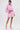 A woman poses confidently in the BUBBLEGUM BUBBLE HEM BOMBER, a light pink zip-up jacket with distressed fringe, paired with a matching mini skirt and platform heels against a plain white background.