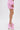 A person stands on a white background wearing BUBBLEGUM BUBBLE HEM SHORTS, styled with high platform pink heels featuring ankle straps and bows. Only the lower body is visible in this textured pink AKIRA Label outfit.