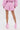 A person stands with legs apart in BUBBLEGUM BUBBLE HEM SHORTS and matching pink platform heels, embracing Barbie Style. Two small thigh tattoos are visible against a plain white background.