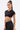 A woman with long dark hair in a high ponytail wears the black TOO SEXY FOR THIS BODYSUIT featuring gold buckle details, styled with bold gold earrings and a cuff bracelet. She stands against a plain white background.