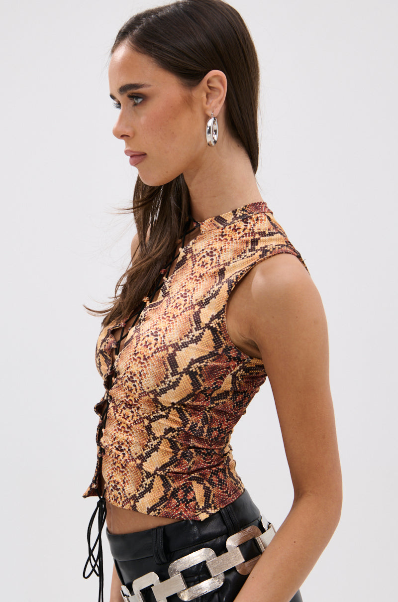A woman with long brown hair wears silver earrings, the curve-hugging RATTLESNAKE LACE UP TOP with a snakeskin pattern, and black pants with a large silver chain belt, shown in profile against a plain light background.