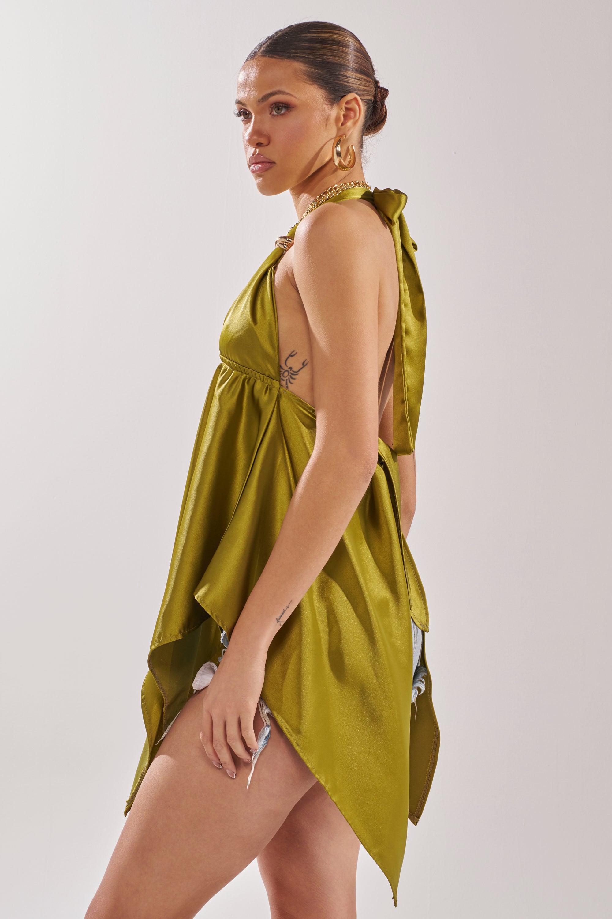 A woman models the LOTS OF LOVE TO GIVE HALTER NECK BLOUSE IN CHARTREUSE with gold hoop earrings and a chunky necklace, showcasing this statement going-out top against a plain white background. 4