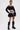 A person with short hair wears the LET IT GO OFF THE SHOULDER BLOUSE in a cropped style, paired with a black mini skirt and knee-high lace-up boots, standing confidently against a plain white background.
