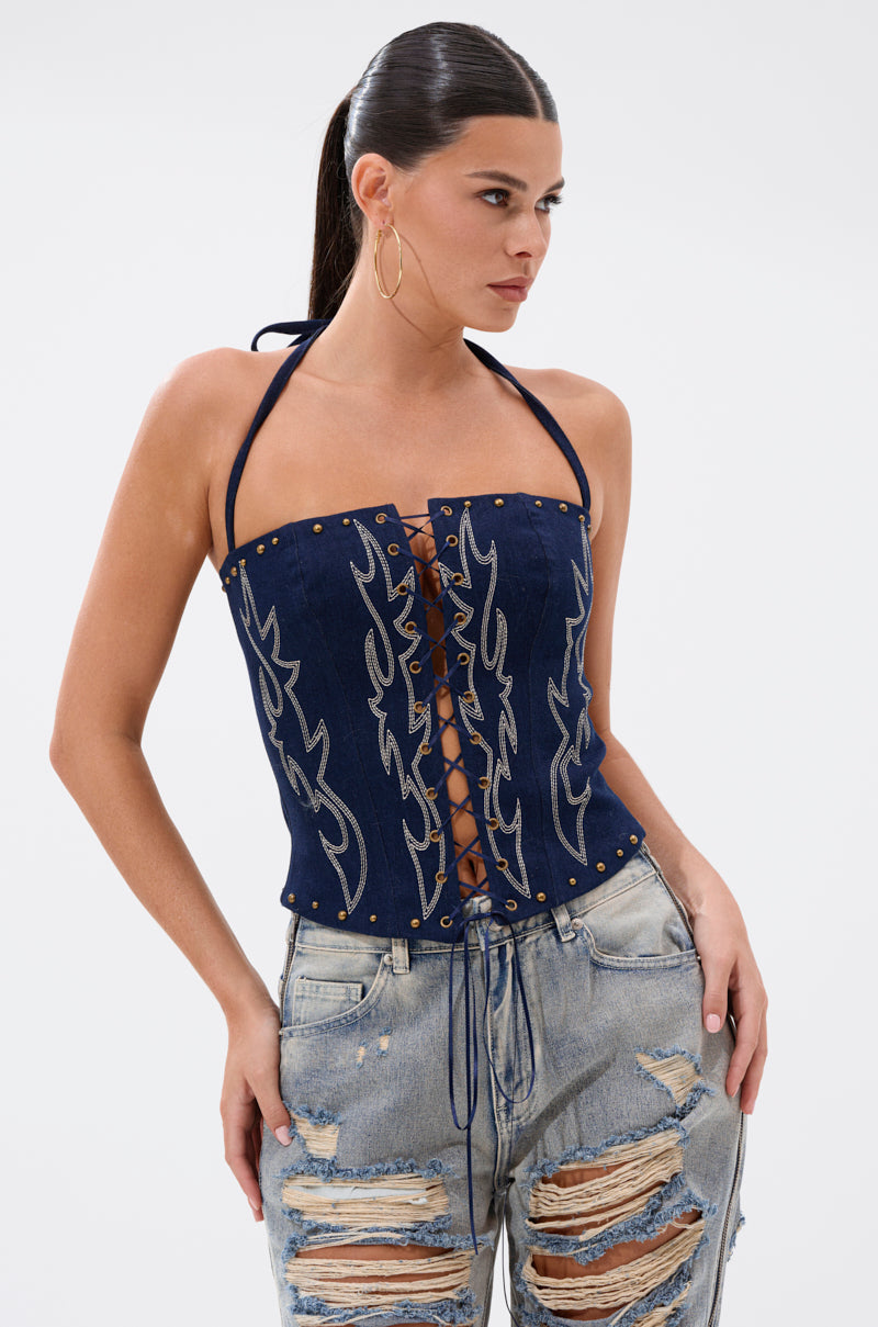 A woman with dark hair in a ponytail wears the KIMMY LACE UP DENIM CORSET and light blue, distressed jeans, standing confidently against a plain white background. 2