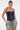 A woman with slicked-back hair and large hoop earrings wears the KIMMY LACE UP DENIM CORSET and light blue ripped jeans, blending casual style with cowgirl corset vibes against a plain white background.