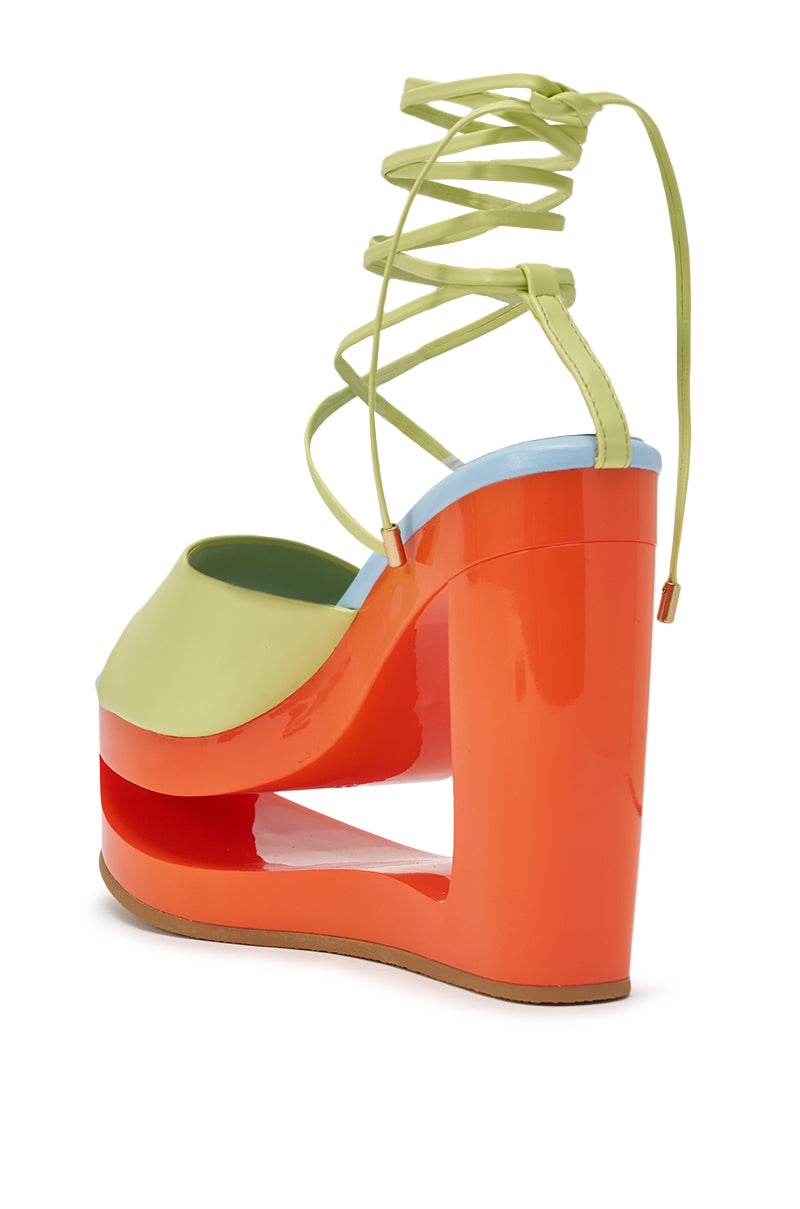The AZALEA WANG TAFFY MULTI NOVELTY WEDGE MULE SANDAL features a glossy orange platform heel, light green upper, sky blue sole trim, and lace-up ankle ties, shown from the back. 5