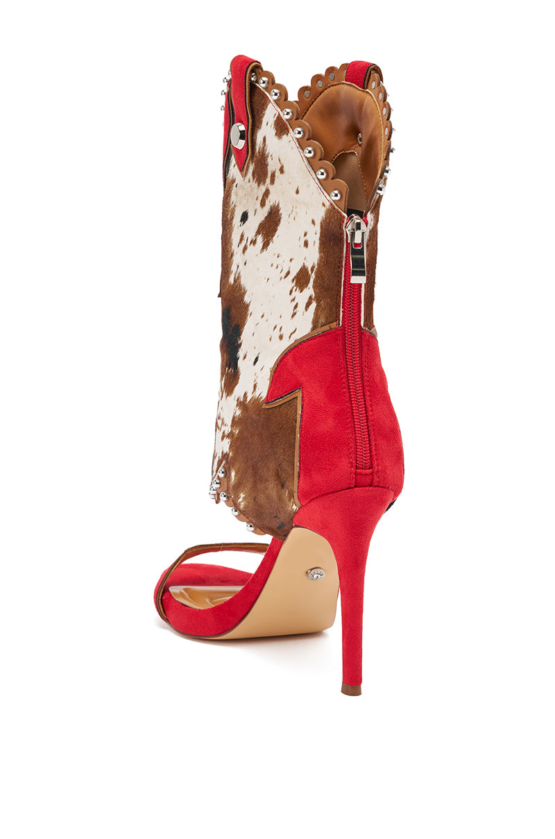 The AZALEA WANG TAHLIE COW MULTI WESTERN GLADIATOR SANDAL blends cowboy boot and stiletto sandal styles, with a red sole, stiletto heel, brown and white cow print shaft, silver studs, and a side zipper. 8