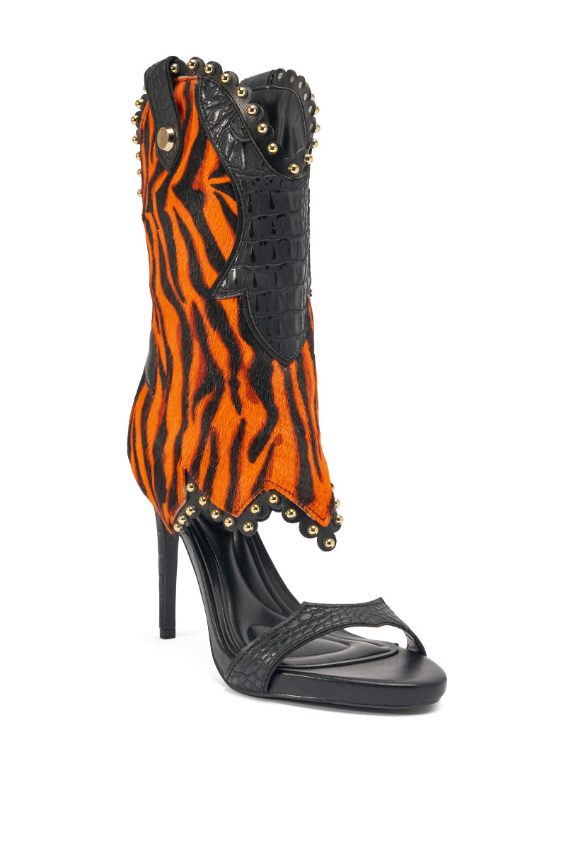 The AZALEA WANG TAHLIE ORANGE MULTI WESTERN GLADIATOR SANDAL features a high heel, black sole, open toe, orange and black tiger-striped upper with gold stud trim and textured black leather accents.
