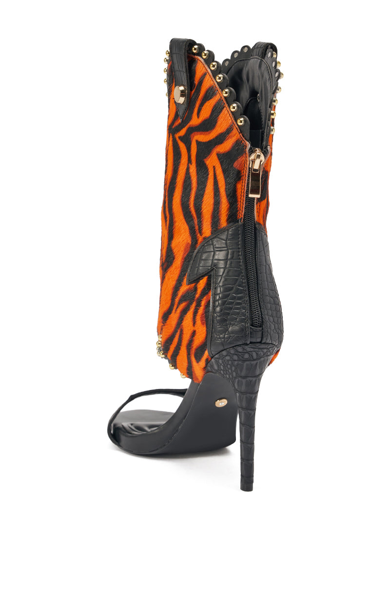 The AZALEA WANG TAHLIE ORANGE MULTI WESTERN GLADIATOR SANDAL features an orange and black tiger-striped upper, black crocodile-textured accents, gold studs, a back zipper, and an open toe for a bold look.