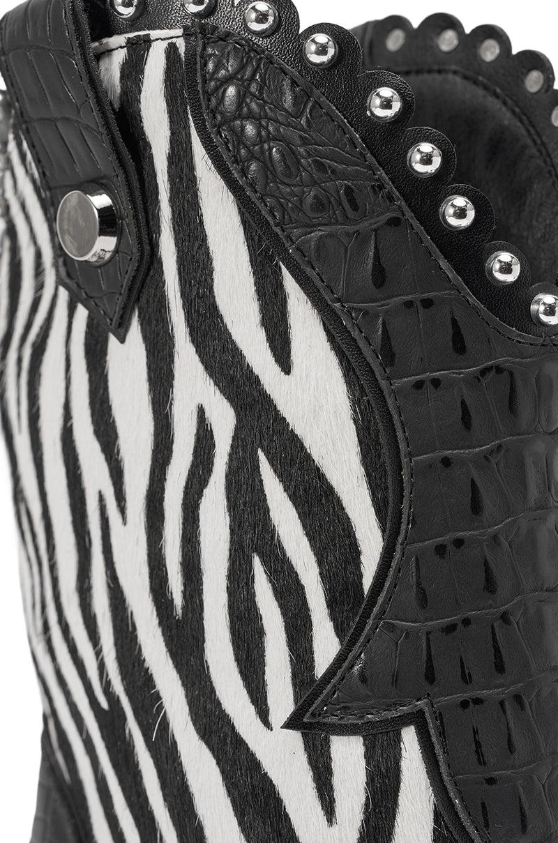Close-up of the AZALEA WANG TAHLIE ZEBRA MULTI WESTERN GLADIATOR SANDAL featuring black and white zebra stripes, textured black leather, silver studs on the top edge, and a decorative side button.