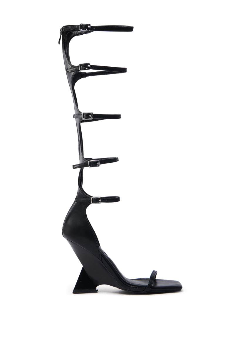 The AZALEA WANG TAITEN BLACK SANDAL is a black, vegan leather high-heeled sandal with a novelty wedge heel and multiple thin straps that extend up the leg, each fastened with small buckles, showcased on a plain white background.
