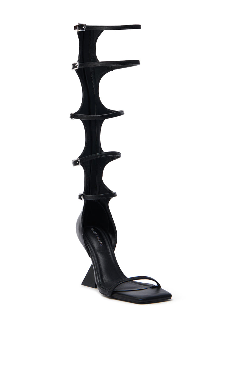 The AZALEA WANG TAITEN BLACK SANDAL is a black high-heeled sandal crafted from vegan leather, featuring multiple thin straps extending up the leg, a square toe, and a geometric heel for a modern look, with a comfort cushion insole for all-day wearability.