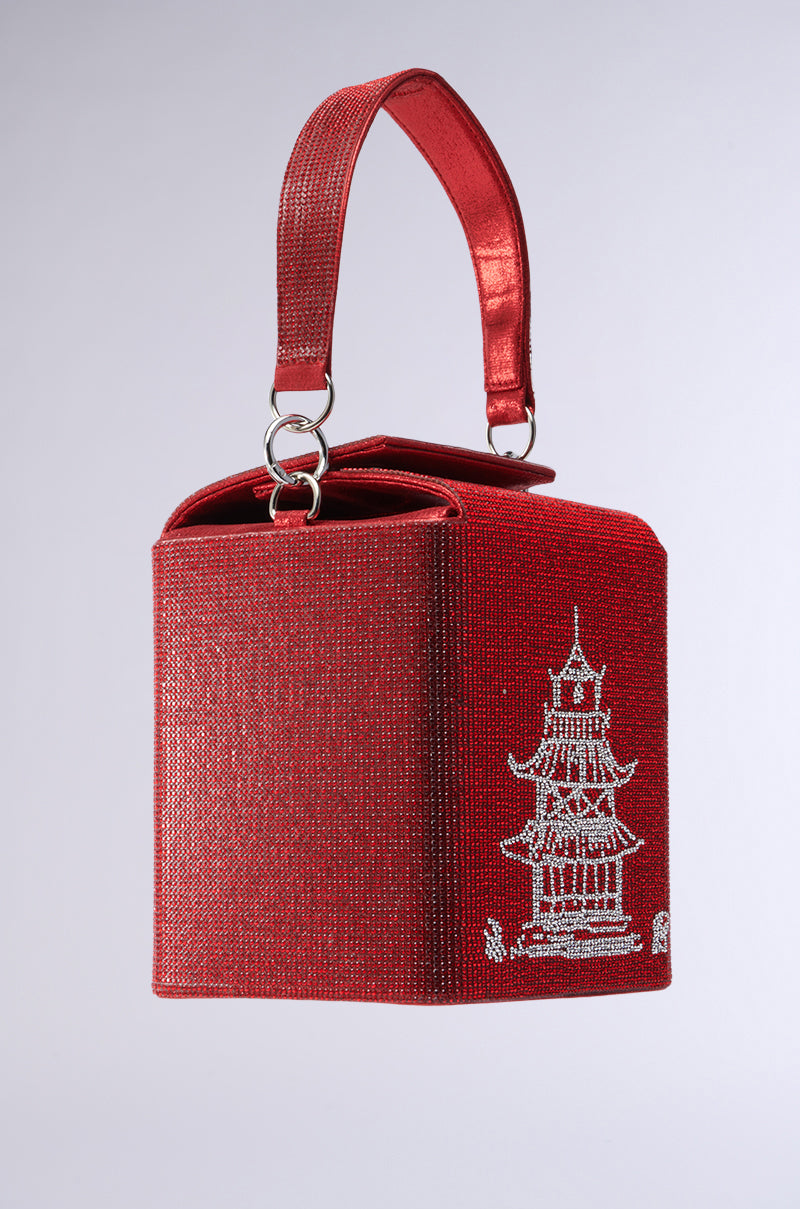 The TAKE ME AWAY BLING BAG is a red, box-shaped handbag adorned with rhinestones, featuring an oriental pagoda design. With its single handle and textured metallic sheen, it's perfect for those who love a standout style.