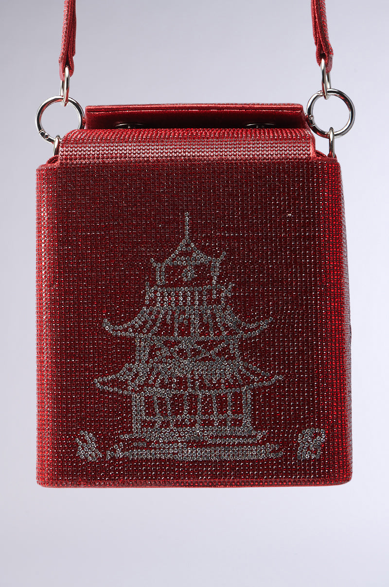 The TAKE ME AWAY BLING BAG is a small red bag with takeout box-inspired graphics, featuring shimmering rhinestone embellishments in a silver pagoda design, and includes a handle with silver rings on a plain white background.
