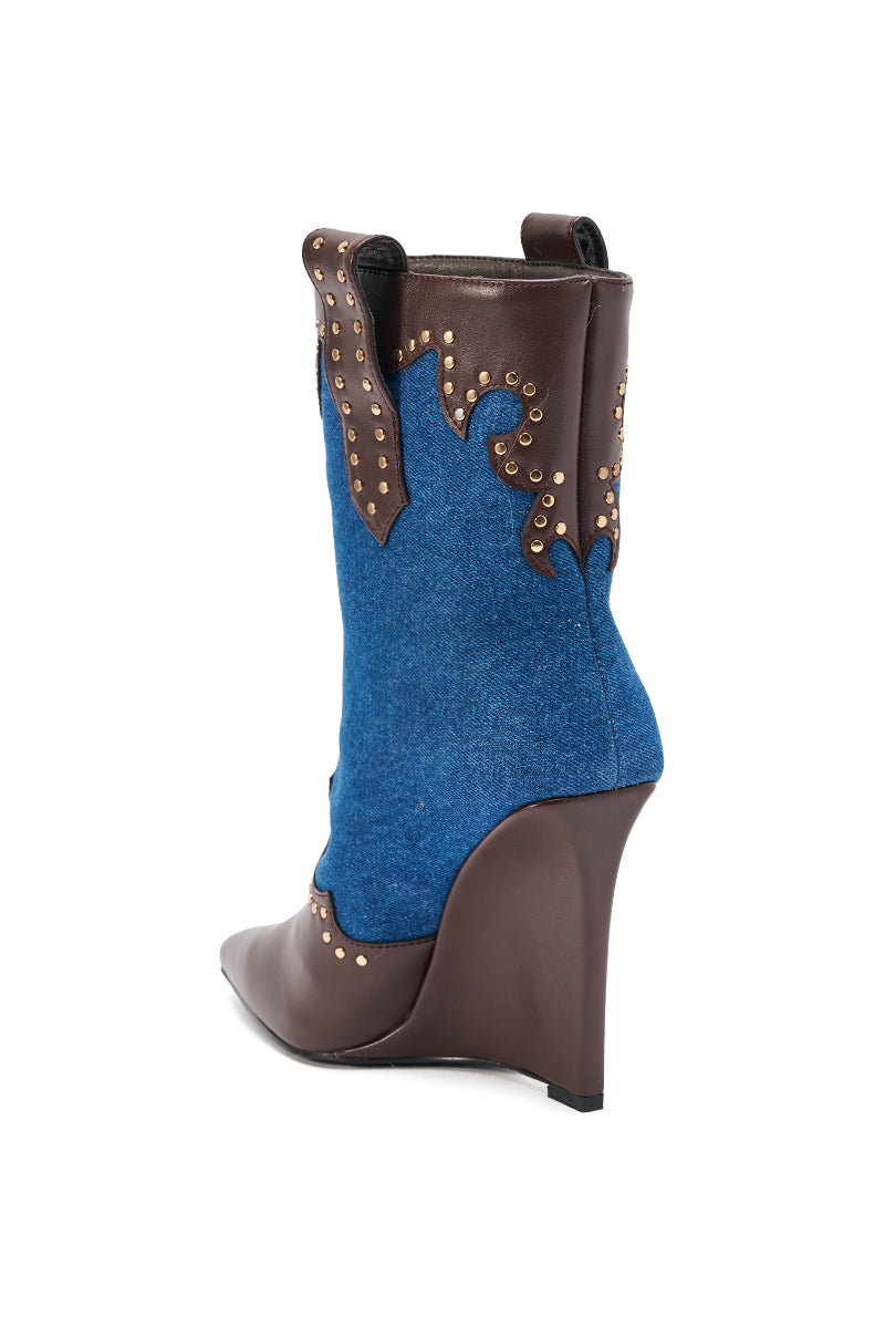The AZALEA WANG TALLULAH DENIM WEDGE WESTERN BOOTIE features a pointed toe, blue denim shaft, faux leather trim with gold studs, brown wedge heel, and Western-inspired design with brown accents.