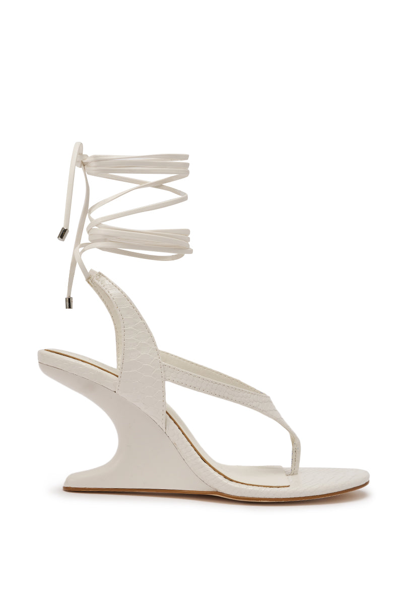 The AZALEA WANG TAMSIN WHITE CROC NOVELTY WEDGE STRAP SANDAL features a sculptural curved wedge heel, crocodile-textured white straps, and long lace-up ankle ties with metal tips, shown in side profile on a white background. 4