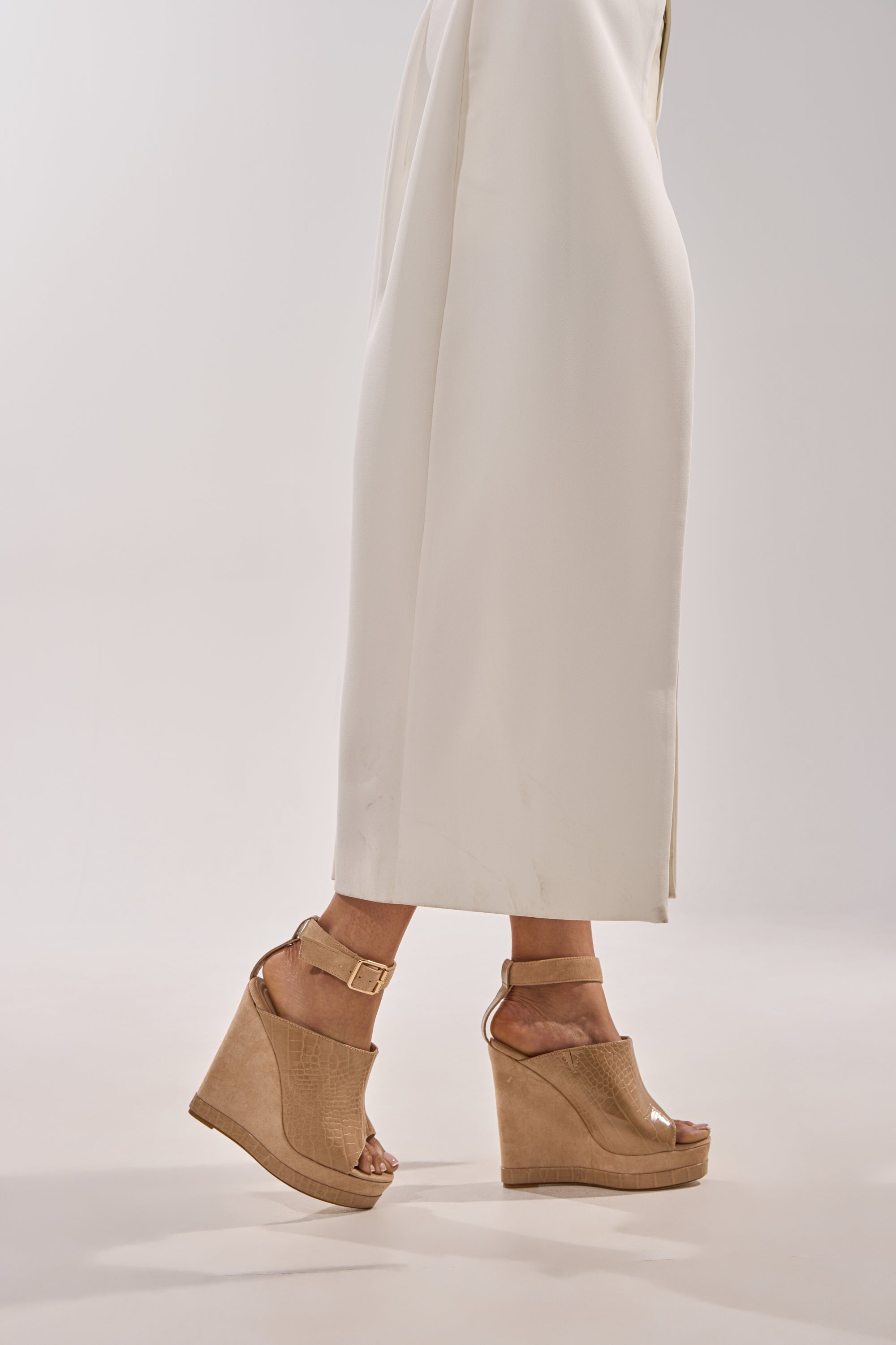 A person walks against a neutral background wearing a long white skirt and the AZALEA WANG TANA NUDE MIXED MATERIAL WEDGE sandals with comfort cushion insoles and ankle straps. 1