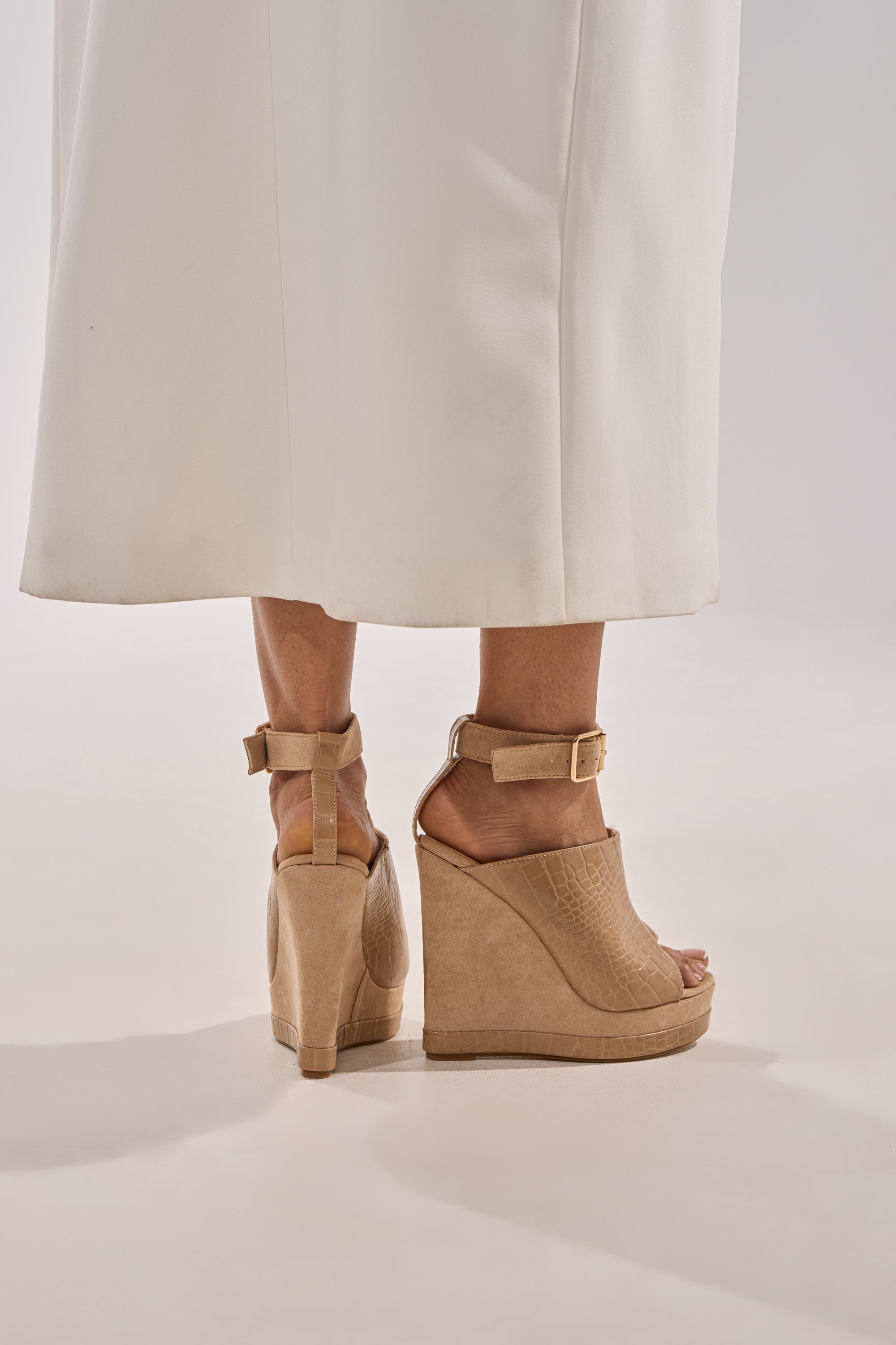 A person wearing a long white skirt and AZALEA WANG TANA NUDE MIXED MATERIAL WEDGE sandals with comfort cushion insoles stands on a light-colored floor, photographed from behind. 2