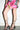 A person wearing a colorful skirt with a large pink flower print, the AZALEA WANG TARANIS black chunky heel lace-up sandals, and bracelets. Their legs are bare, showing a detailed flower tattoo on their upper thigh.