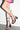 A person wearing a pink patterned skirt and the AZALEA WANG TARANIS Black Curved Chunky Heel Lace Up Sandals stands against a white wall.
