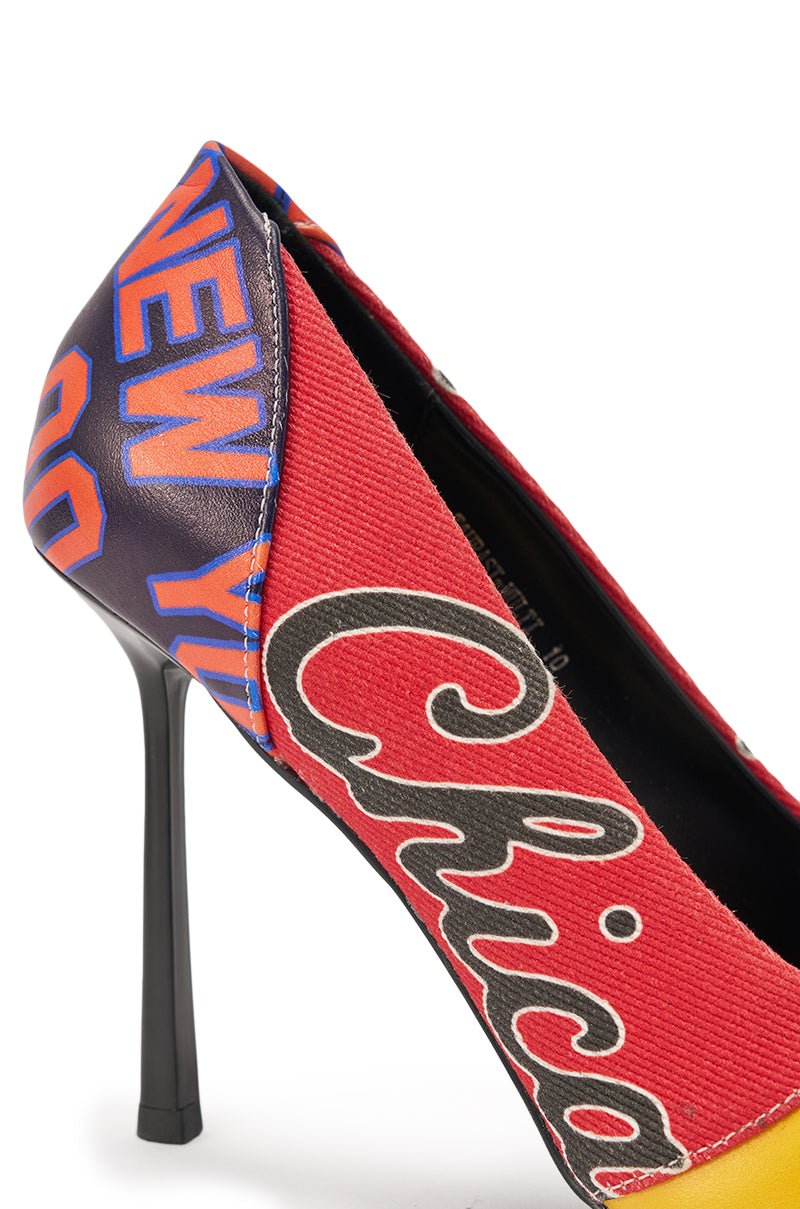 The AZALEA WANG MULTI PRINTED STILETTO POINTED TOE PUMP features a comfort cushion insole and bold "Chicago" and "New York" graphic text on a vibrant red and purple background. 7