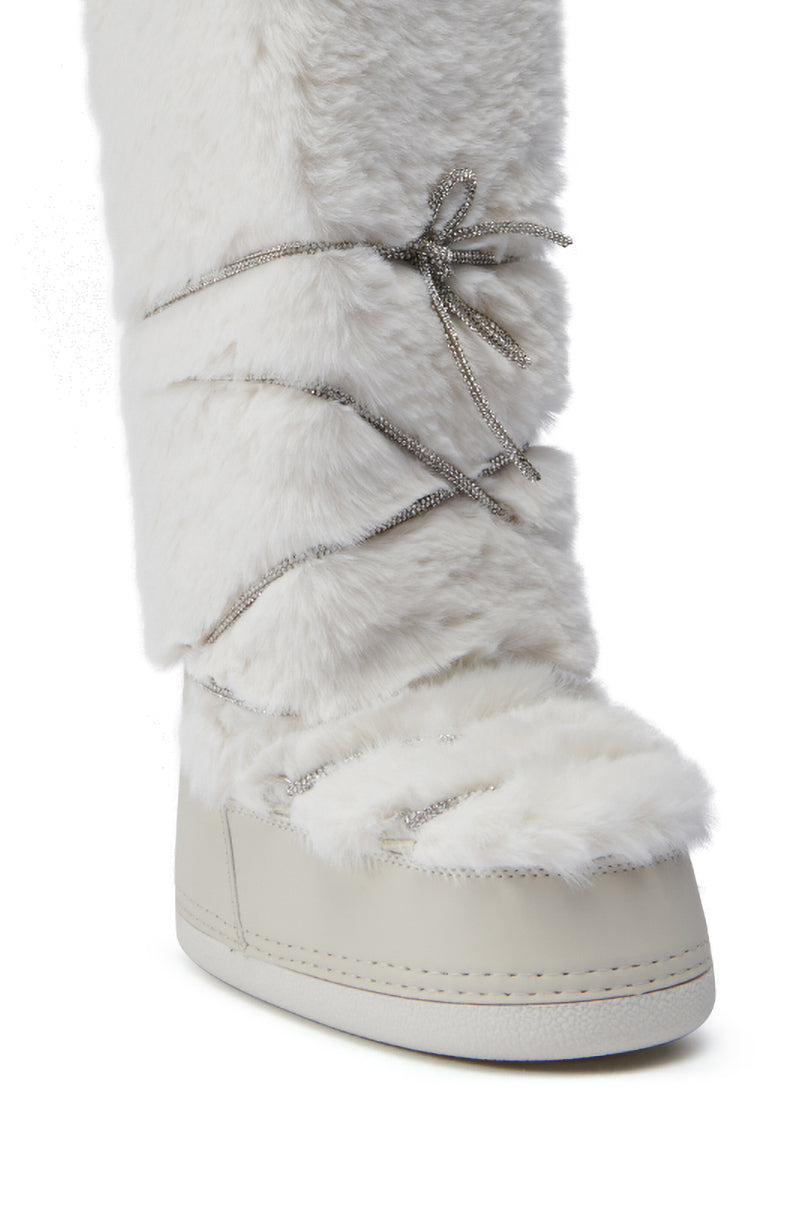 A detailed shot of the AZALEA WANG TAYTON Beige Fuzzy Flat Knee High Boot showcases its plush, faux fur texture and decorative silver laces wrapped around the shaft. With a flat sole, this boot is perfect for cold weather.