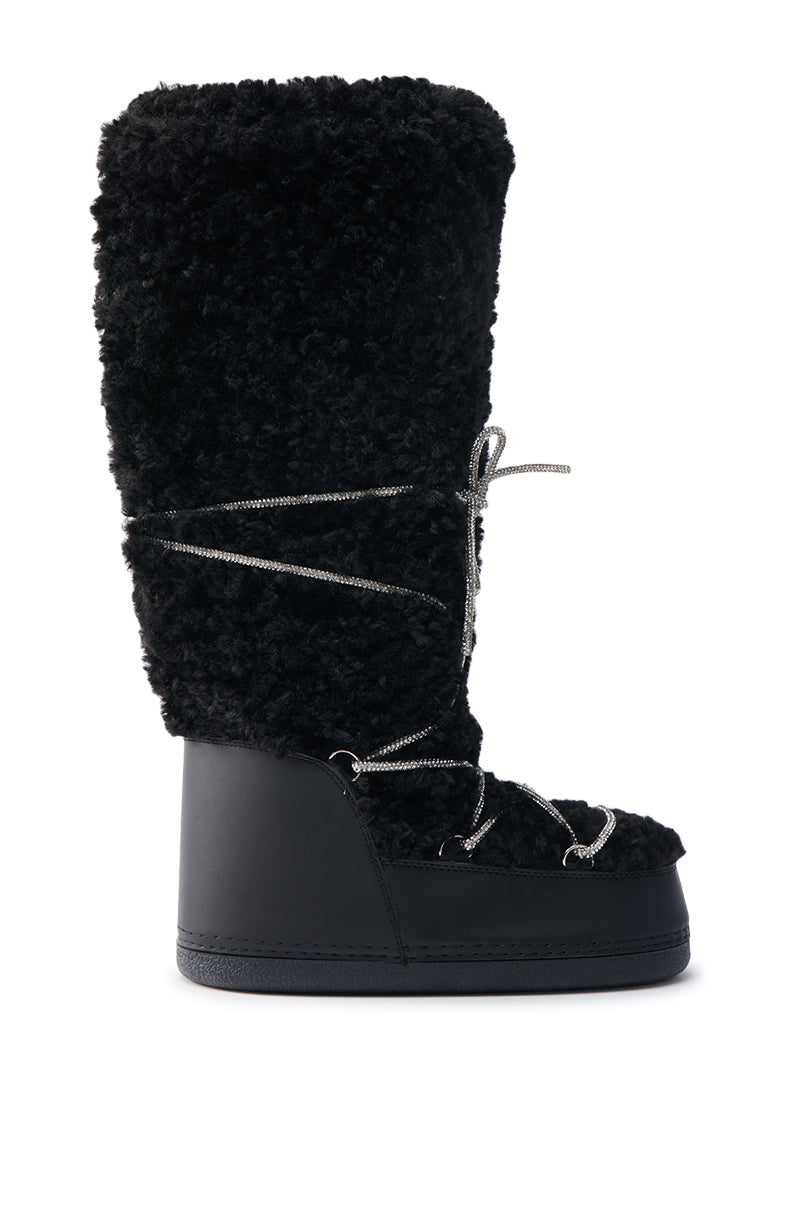 The AZALEA WANG TAYTON black knee-high furry boot features a fluffy exterior and flat sole, with elegant silver laces crisscrossing along the front for a cozy yet stylish design.
