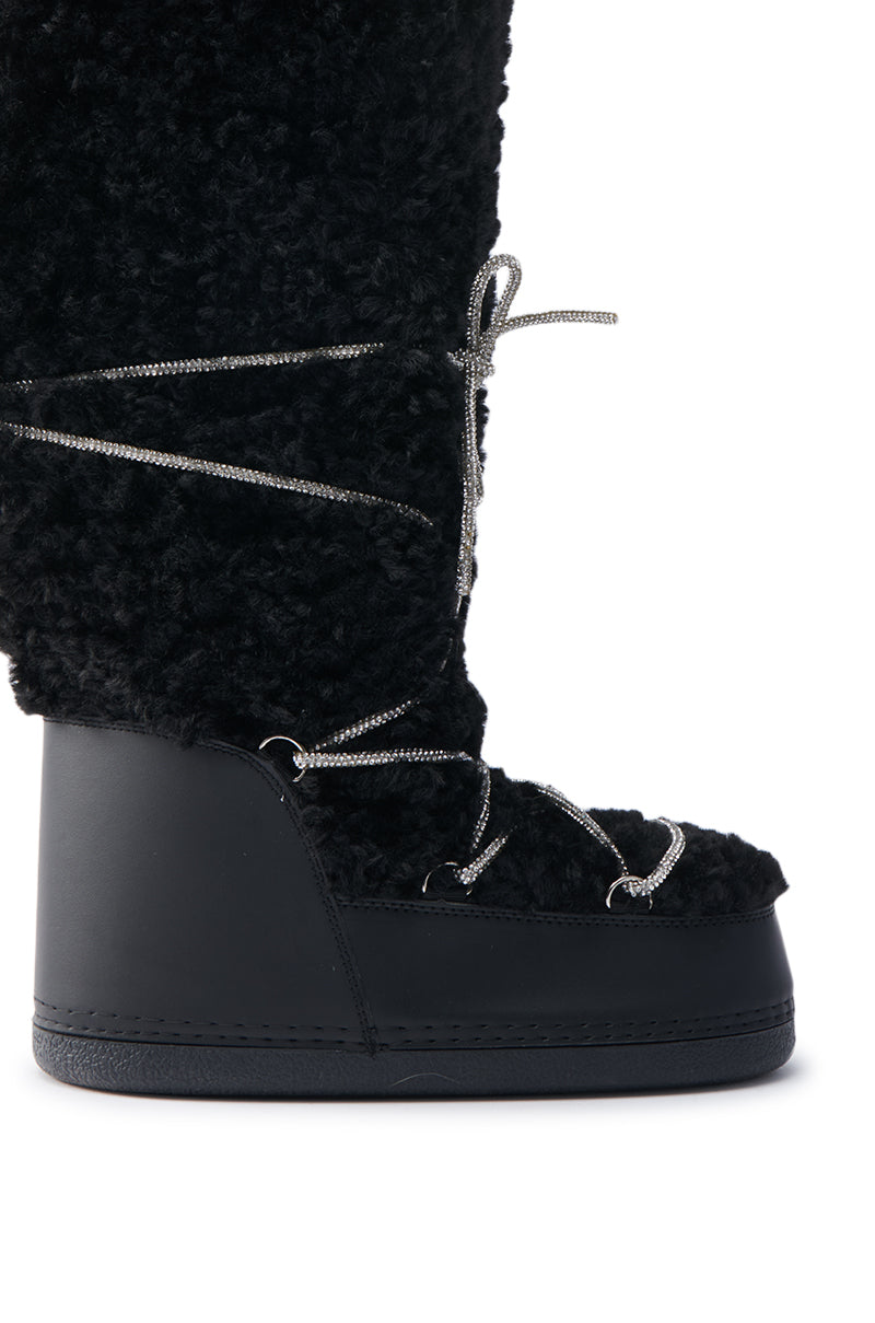 The AZALEA WANG TAYTON Black Knee High Furry Boot showcases a plush, fuzzy surface with shiny metallic laces. It features a high platform sole and extends up the leg, combining modern design with faux sherpa charm.
