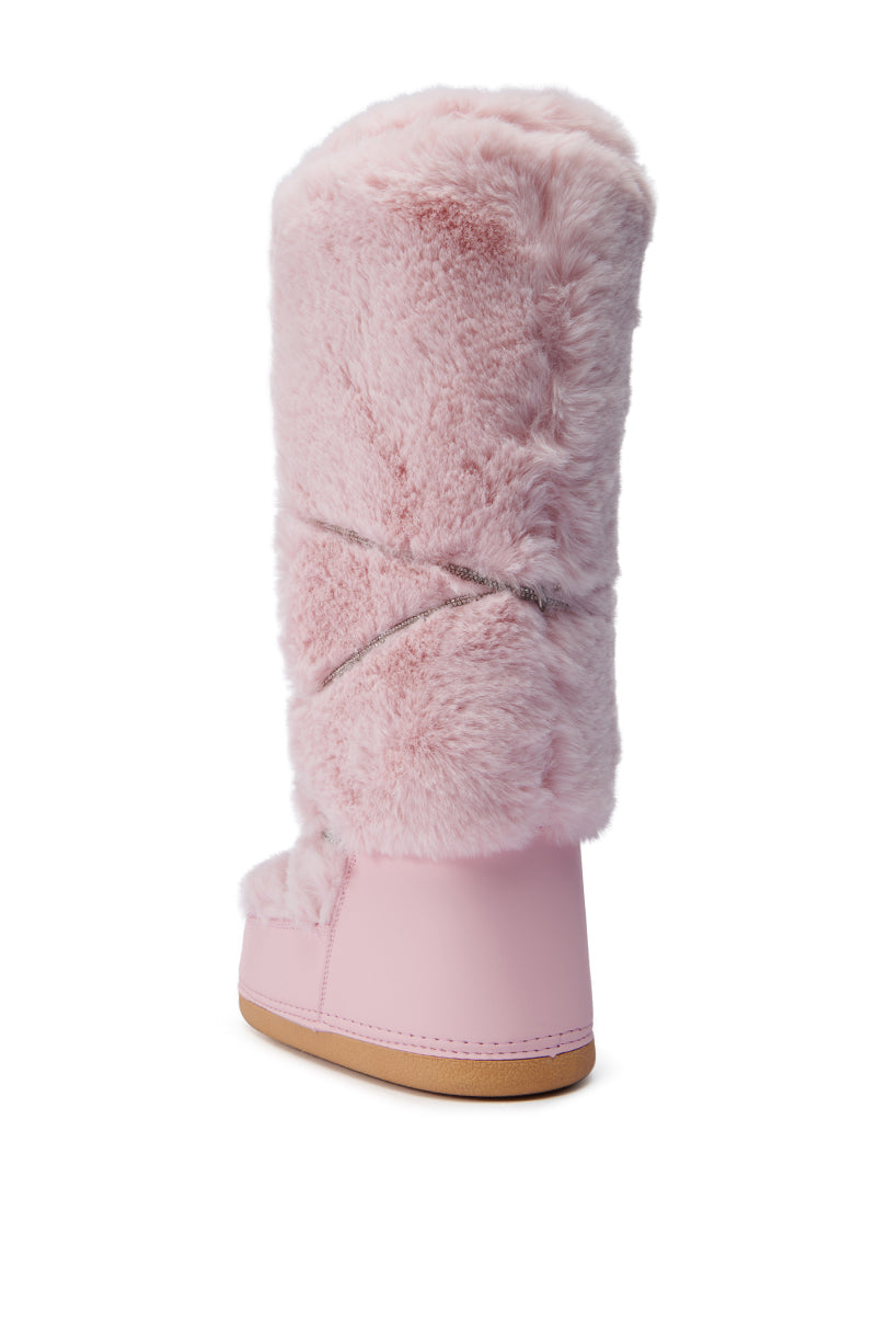 The AZALEA WANG TAYTON PINK FUZZY FLAT KNEE HIGH BOOT is depicted from an angle, showcasing its plush and soft material. It features a decorative crisscross detail, and its light brown flat sole stands out against the white background.
