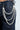 A person wears dark jeans with a stylish "STYLE ME UP PEARL PANTS CHAIN," featuring faux pearl strands and lobster claw closures. The large pearls drape elegantly, creating a striking contrast against the denim.