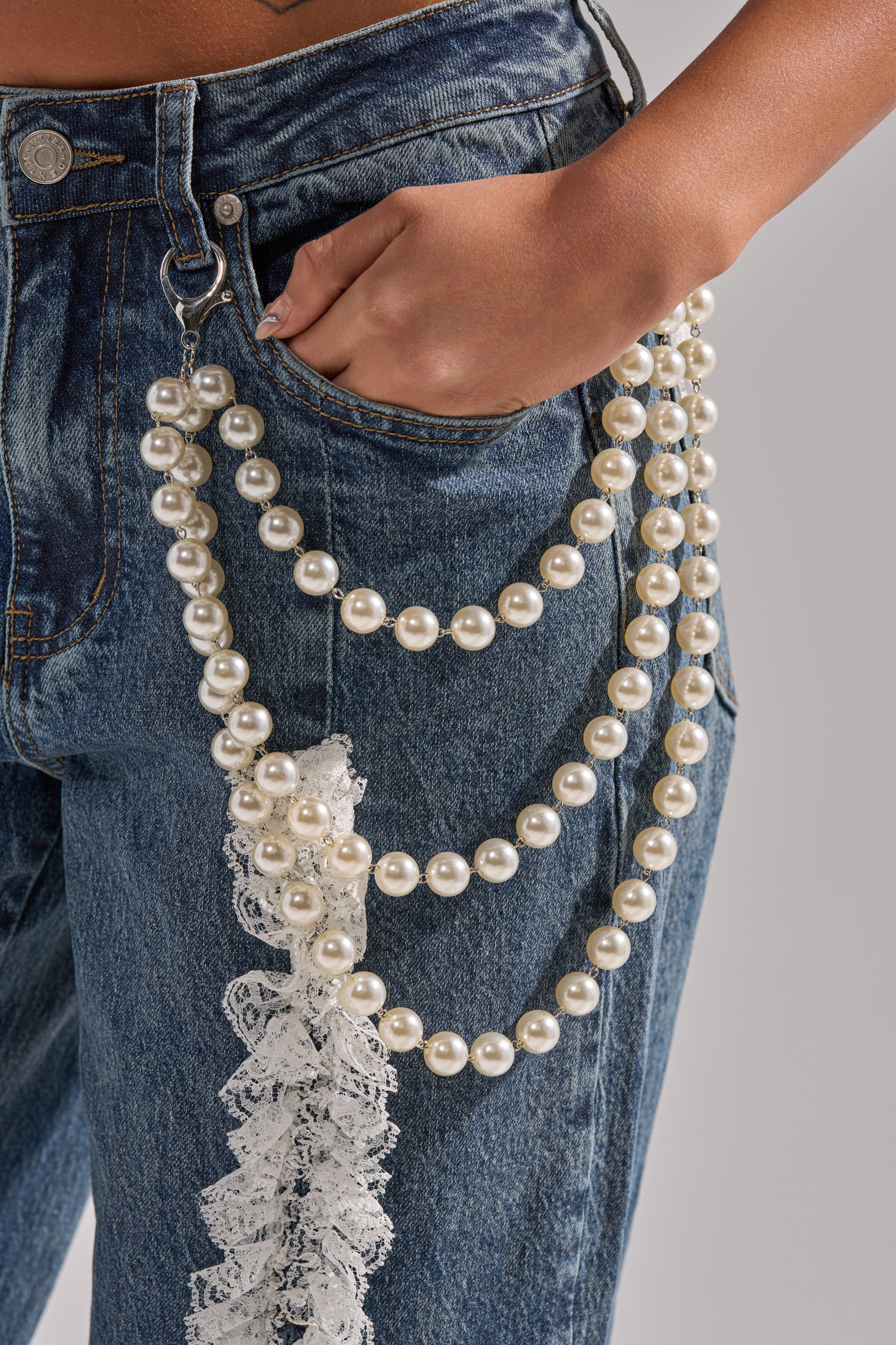 A person models blue jeans accessorized with the STYLE ME UP PEARL PANTS CHAIN—a layered faux pearl belt chain draped from the belt loop to the front pocket—hand casually resting in the pocket.