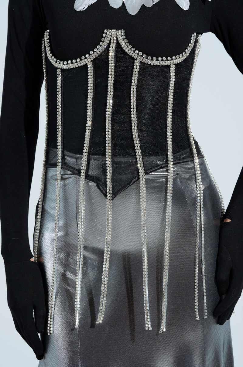 A person's torso displays the CRYSTALIZING BLING UNDERBUST BELT, adorned with beaded vertical lines and rhinestone trim over a metallic silver outfit. It elegantly cinches the waist, complemented by sleek black clothing beneath, enhancing the chic ensemble.