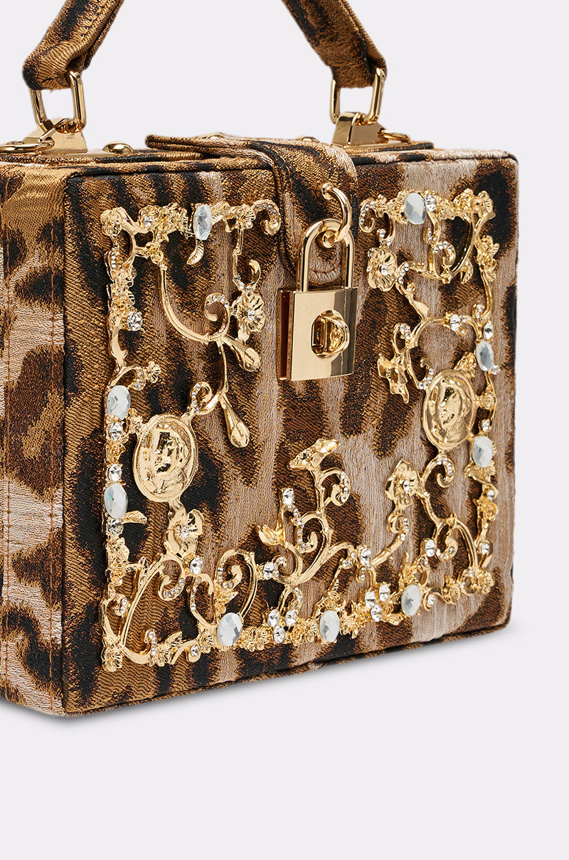The DOLCE CHEETAH PURSE is a rectangular luxury handbag with vibrant leopard-print fabric, gold-tone hardware, a top handle, ornate gold and crystal front embellishments, and a decorative gold lock.
