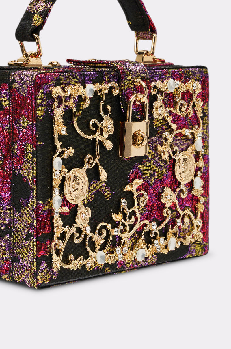 The BIG MONEY TRUNK BAG is a small handbag with a floral pink, purple, and gold fabric, ornate gold metalwork, pearl accents, top handle, and gold clasp lock—a true luxury purse.
