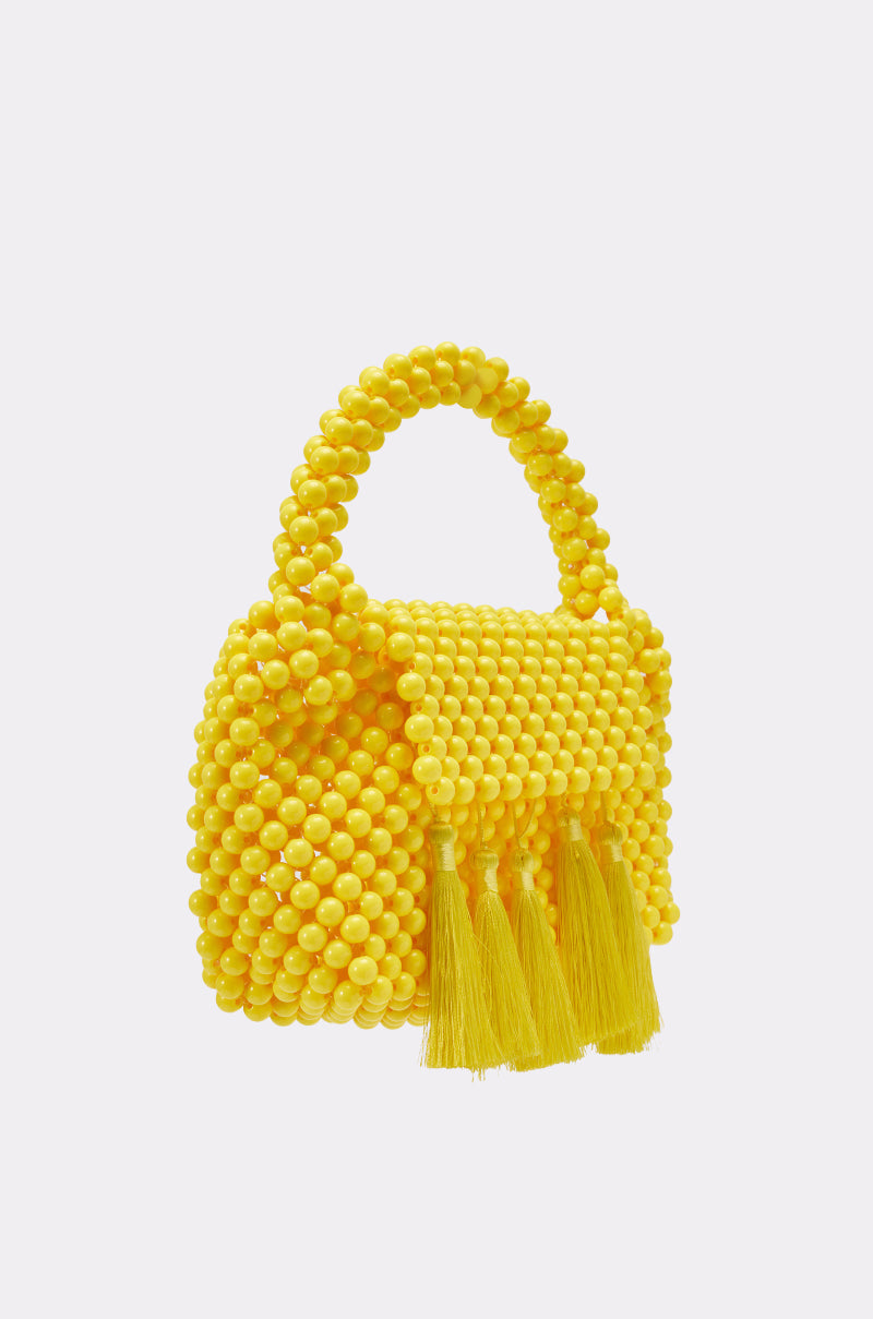 The IN THE SUN BEADED BAG features bright yellow resin beads, a top handle, and four tassels for playful texture—perfect as a cheerful summer vacation accessory against any outfit. 2