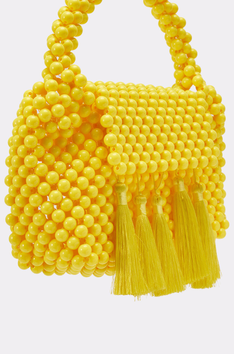 The IN THE SUN BEADED BAG is a small yellow handbag featuring a beaded handle and five tassels, creating a playful fringe detail—perfect as a vibrant summer purse. 3