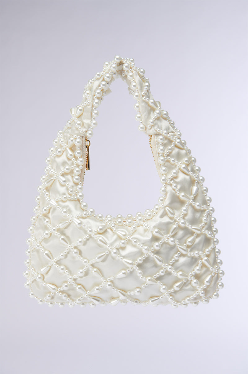 The OLD MONEY PEARL EMBELLISHED PURSE is a stylish satin bag with a padded, quilted design covered in cream-colored fabric, adorned with faux pearl beading at the intersections. The handle is also embellished with pearls, and the bag features a light gold zipper closure.