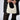 A person wearing a pinstriped blazer over a crocheted top and black lace flared pants is holding an OLD MONEY PEARL EMBELLISHED PURSE. The small, white satin bag features faux pearl beading and a braided handle, while the person's face remains out of sight.