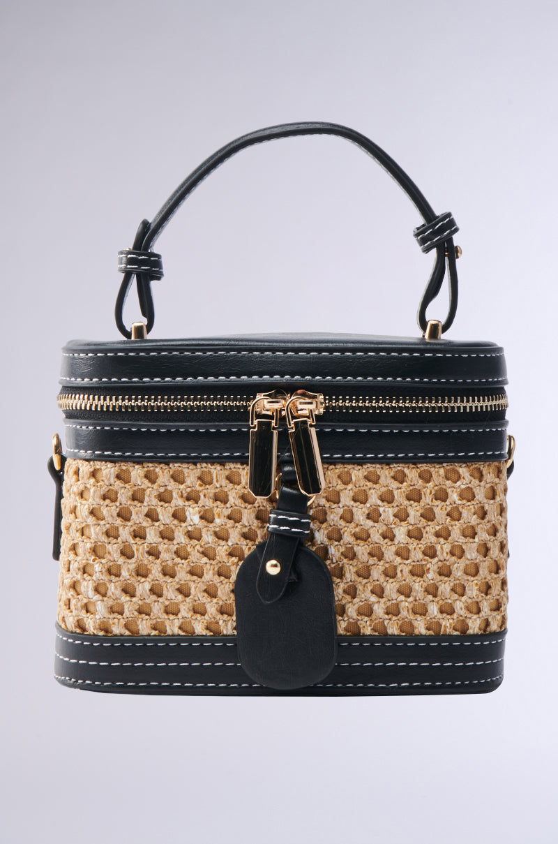 The TAKE ME OUT WICKER PURSE is a stylish, small rattan handbag with a woven straw design, faux leather trim, zip closure with gold hardware, top handle, white stitching details, and an attached front tag.