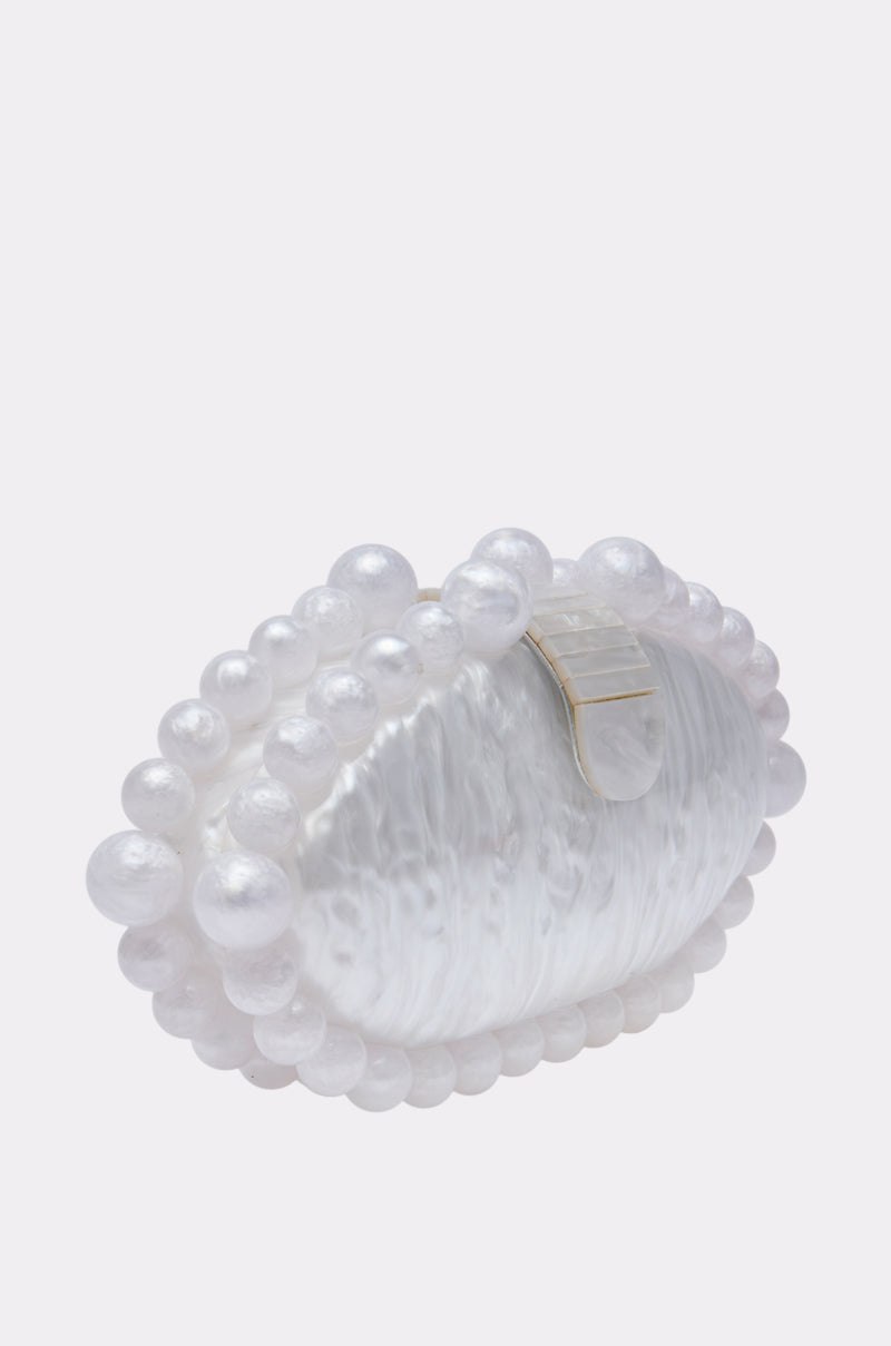 The EXPENSIVE TASTE CLUTCH is a white, oval evening bag with a textured opalescent finish, adorned with large pearl beads along the edges and finished with an elegant gold top clasp. 2