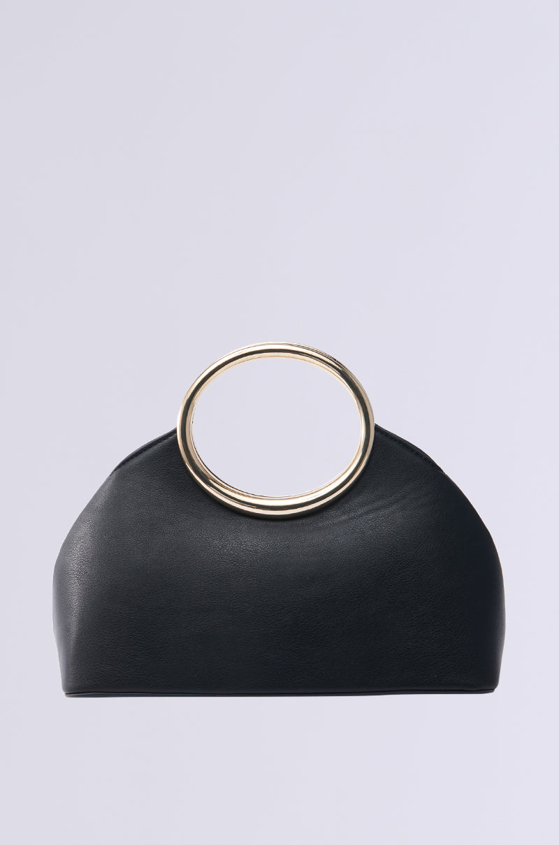 A sleek black faux leather handbag with a minimalist design, featuring a large circular gold handle on top. The I AM LUXE PURSE embodies quiet luxury, set against a plain light gray background. 0