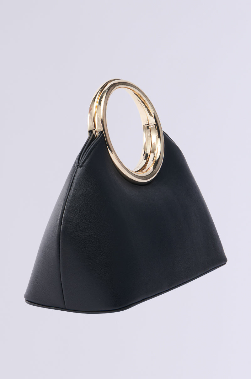 The I AM LUXE PURSE is a black, triangular faux leather handbag with two shiny gold circular handles, boasting a smooth texture. Placed on a plain white background, it highlights an elegant and minimalist design.