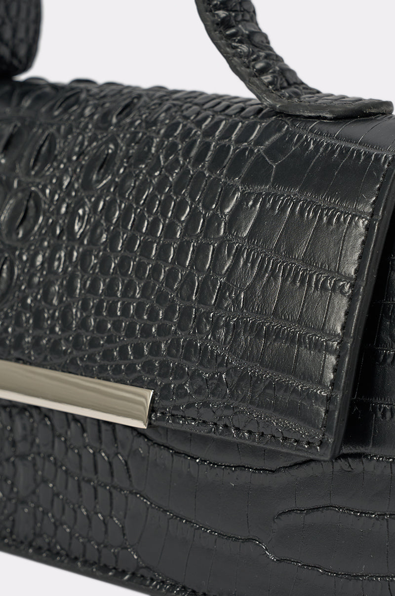Close-up of the VILLAIN ERA PURSE, a black croc-embossed handbag featuring a textured crocodile pattern, rectangular metal accent on the flap, and a matching handle. 3
