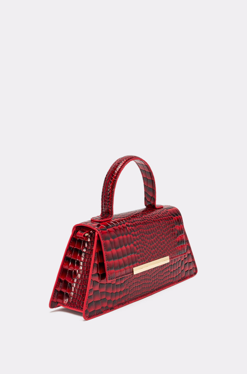 The DAY FAUX CROC PURSE is a small cherry red handbag with a crocodile-patterned vegan leather finish, a gold rectangular front accent, and a single curved handle, shown against a plain white background. 1