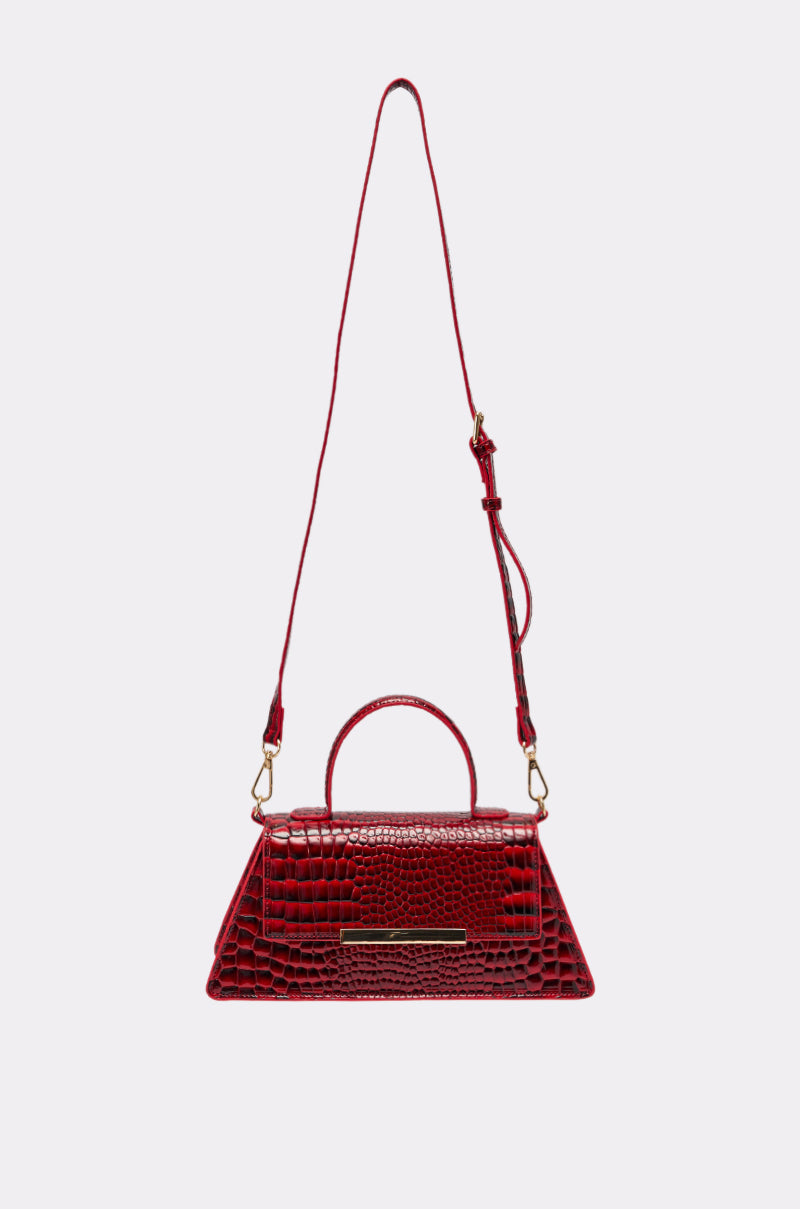 The DAY FAUX CROC PURSE is a small, shiny cherry red handbag made from vegan crocodile leather, featuring a top handle and an adjustable shoulder strap, displayed on a plain light background.