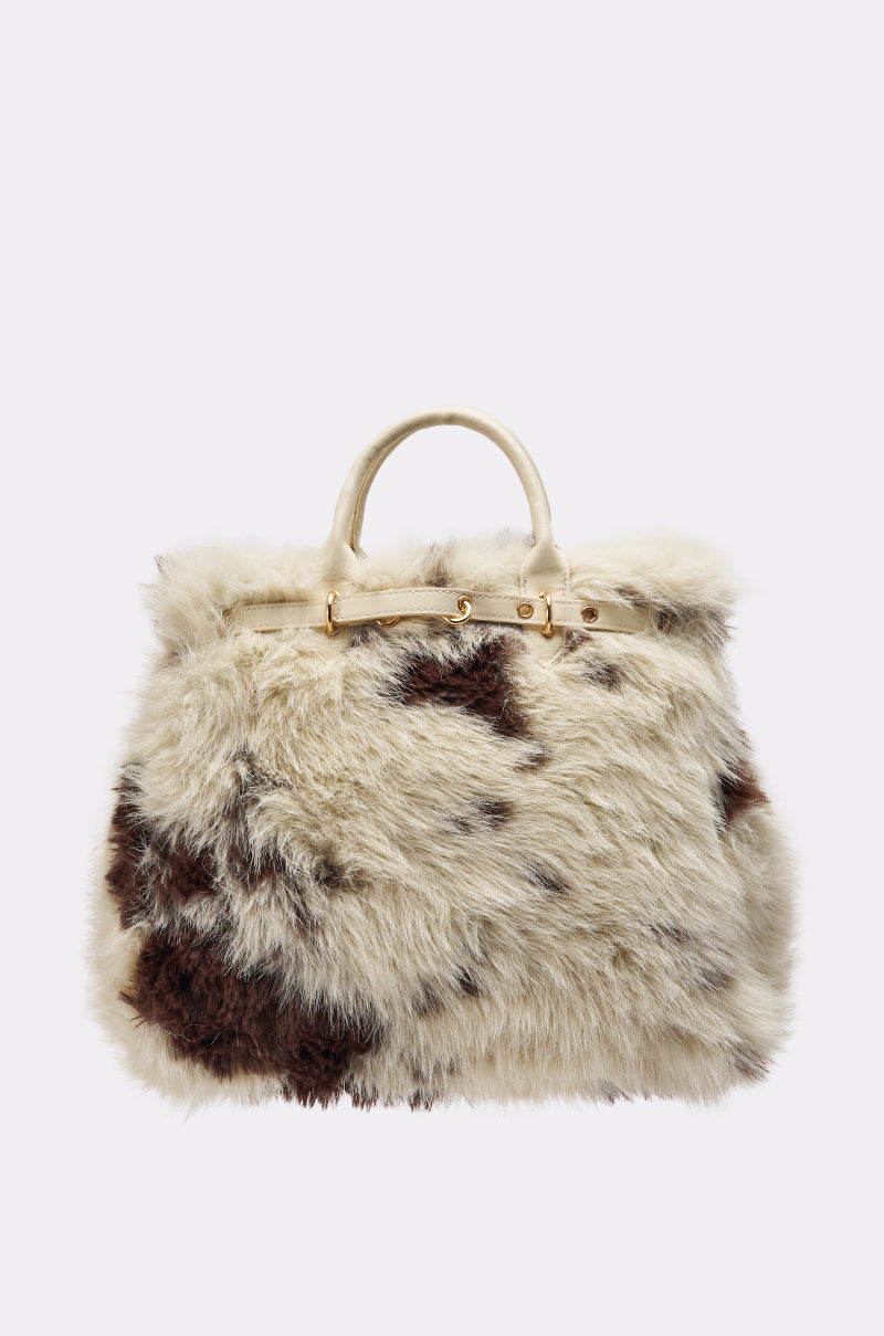 The MOO FAUX FUR MINI TOTE features short handles, fluffy cream faux fur with irregular dark brown cow print spots, and gold hardware.