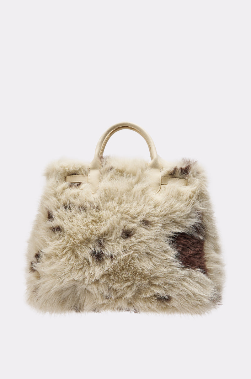 The MOO FAUX FUR MINI TOTE is a cream faux fur mini tote with brown cow print patches, two top handles, and is an adorable AKIRA Label accessory perfect for any look.