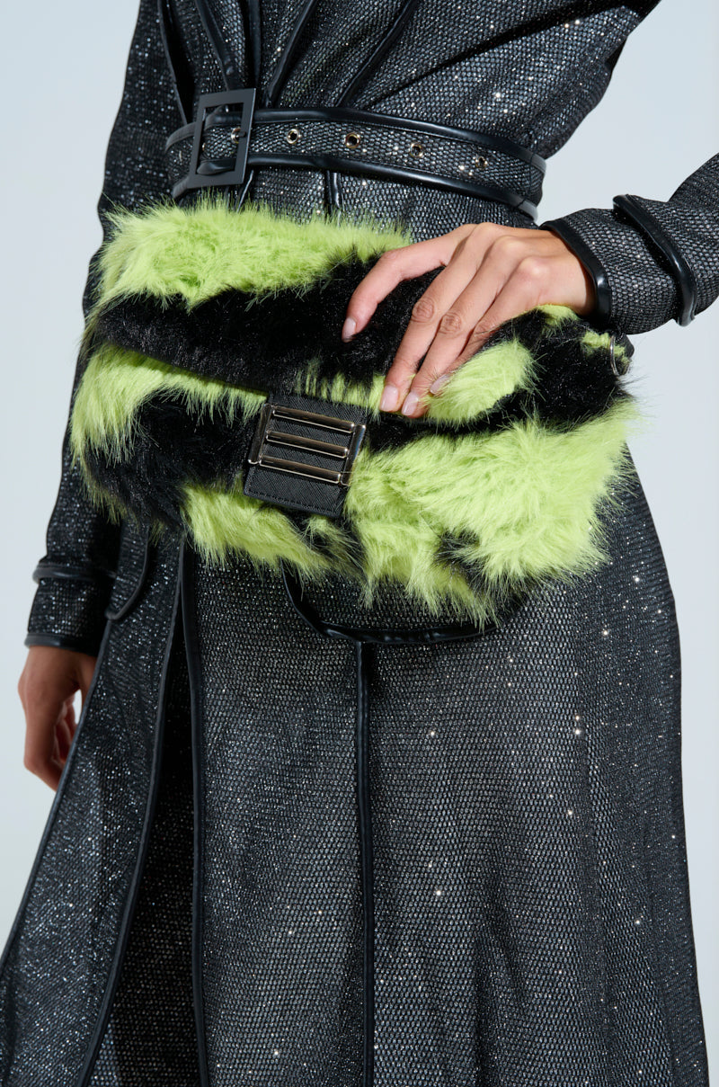 A person in a shimmering dark coat with a wide belt holds a WILD DREAMS ZEBRA FAUX FUR PURSE. Their hand showcases intricate designs, likely henna. The scene offers a close-up of the outfit's textures and details.