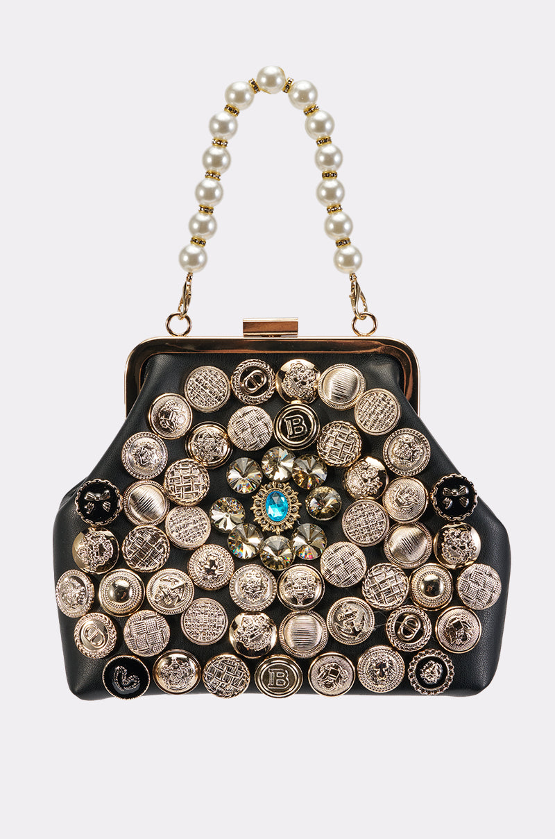 The GEM QUEEN BAG is a black faux leather mini bag featuring a pearl handle, adorned with multiple gold and silver buttons and highlighted by a central blue gemstone accent.