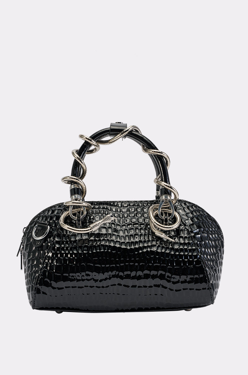 The COME AND GET IT PURSE IN BLACK is a black faux leather handbag embossed with a snakeskin pattern, featuring shiny silver snake-shaped handles and a zippered closure, displayed against a plain white background.